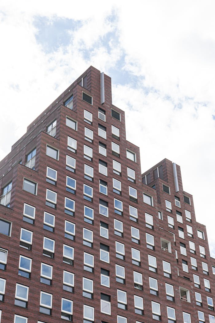 Low angle view of a modern brick building in Amsterdam against a cloudy sky.